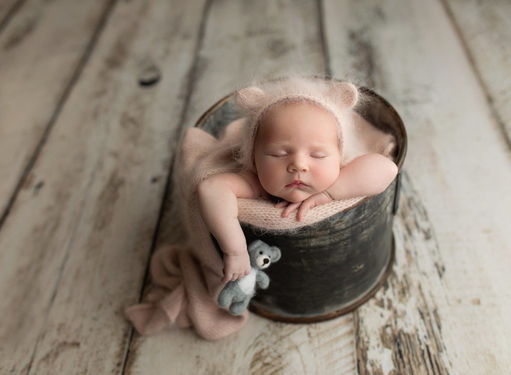 best studio baby pictures, baby girl in bear cap sleeping in bucket with gray teddy bear prop